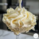 Close-up of fluffy Swiss meringue buttercream frosting on a mixer whisk.