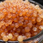 Close-up of guava caviar, small translucent pink spheres in a glass container.