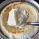 Close-up view of two creamy white substances, possibly whipped cream and crème fraîche, swirled together in a metal bowl.