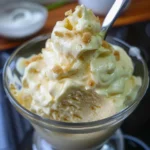 Close-up of a spatula lifting creamy, off-white frosting from a metal bowl.