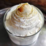 Creamy white substance, possibly whipped cream or frosting, in a metal bowl.