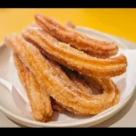 A plate of freshly made churros dusted with cinnamon sugar.