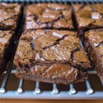 Close-up view of several dark chocolate brownie cookies cooling on a wire rack.