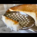 Close-up of a perforated metal spoon resting on a light-colored surface.