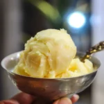 Close-up of a scoop of creamy pineapple ice cream in a metal bowl.