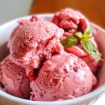 Close-up of three scoops of pink strawberry, yogurt, and rose sorbet in a white bowl.